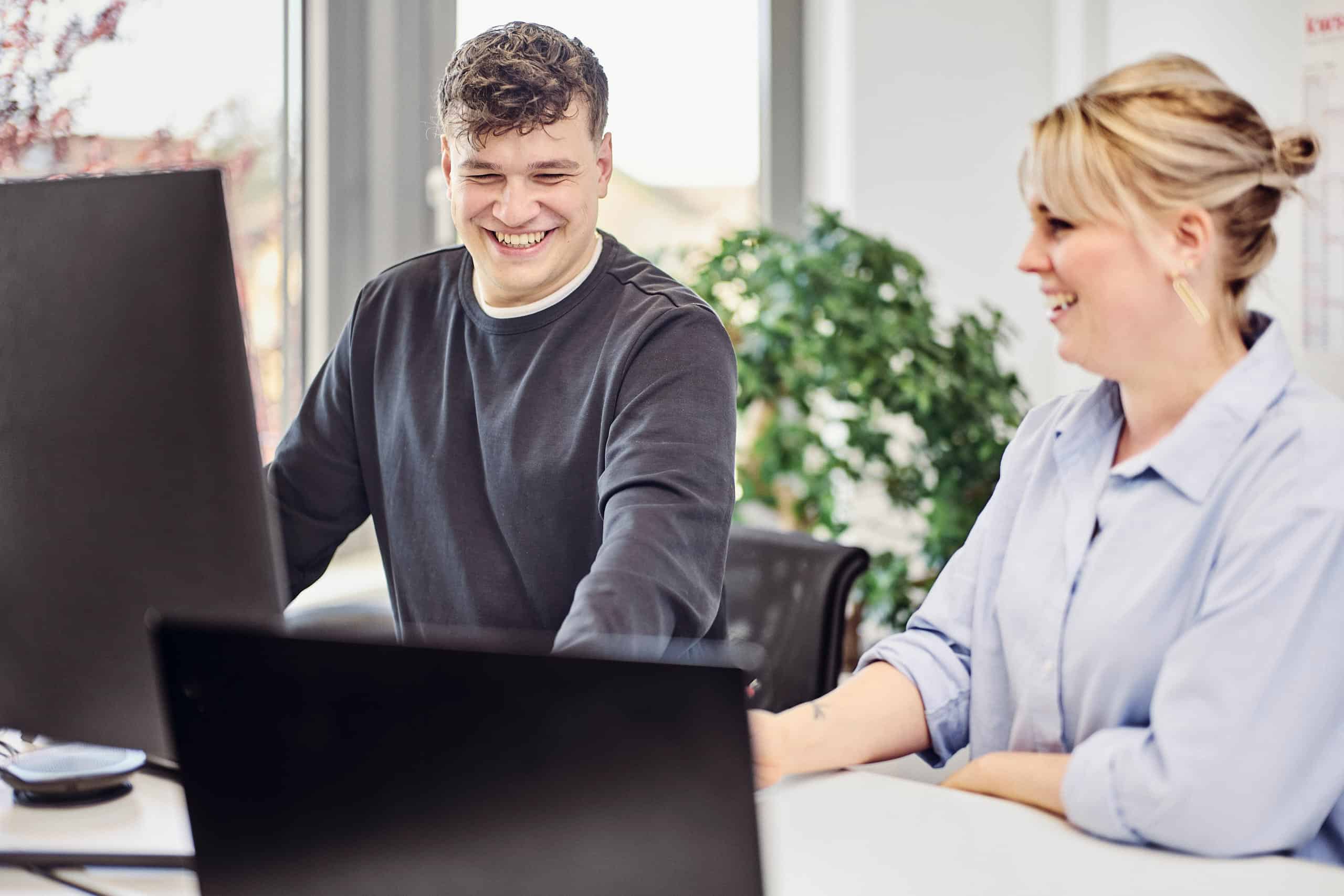 Eine Frau und ein Mann sitzen zusammen an einem PC und lachen